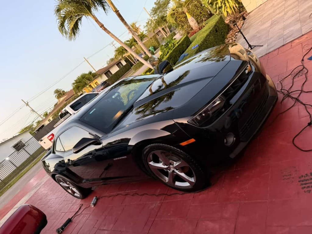 Black Chevrolet Camaro with palm tree reflections and warm sunset light, dynamic angle