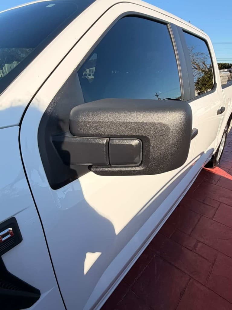 White Ford F-150 driver side mirror and door in sunlight on red driveway